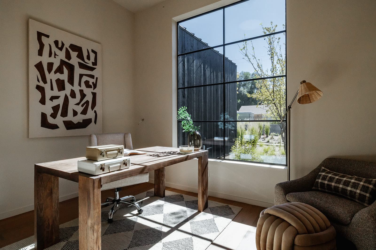 Styled study with a reclaimed timber desk and a graphic canvas beside a steel-framed window.